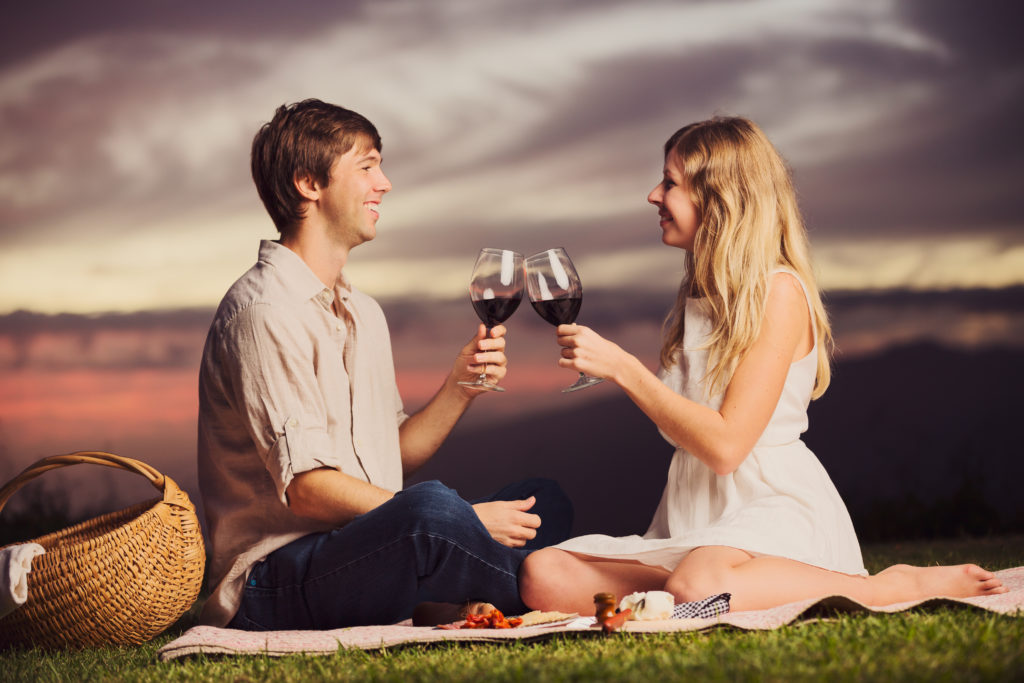 Attractive couple drinking glass of wine on romantic sunset picn